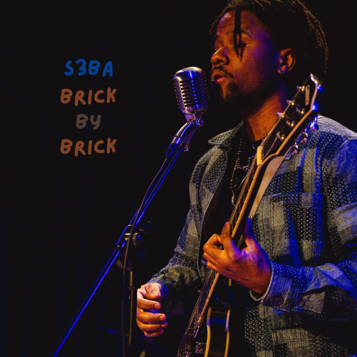Brick by Brick cover art: S3BA singing into a vintage microphone with a guitar under blue stage light, the title hand-lettered beside him.